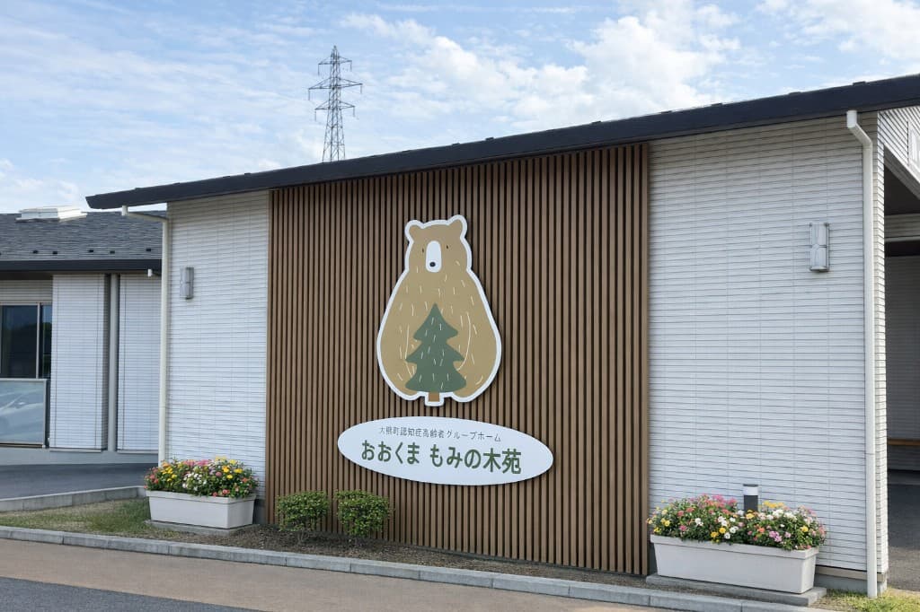 大熊町認知症高齢者グループホームおおくまもみの木苑の外観。くまと木のロゴ看板が掲げられた建物。